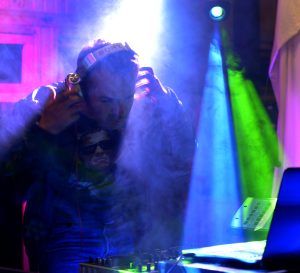 DJ Diego Sánchez en cabina quitándose los audífonos con iluminación artística y visos de colores.