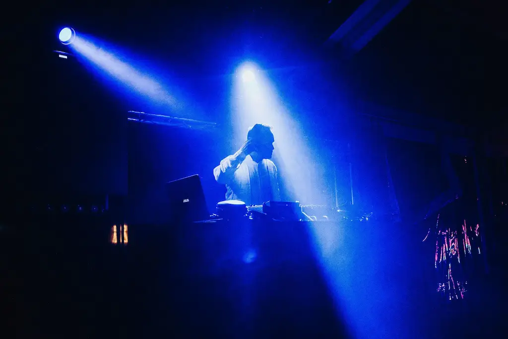 Wedding DJ in Colombia performing on stage, captured in silhouette with blue lighting, focused on precise mixing and crowd control